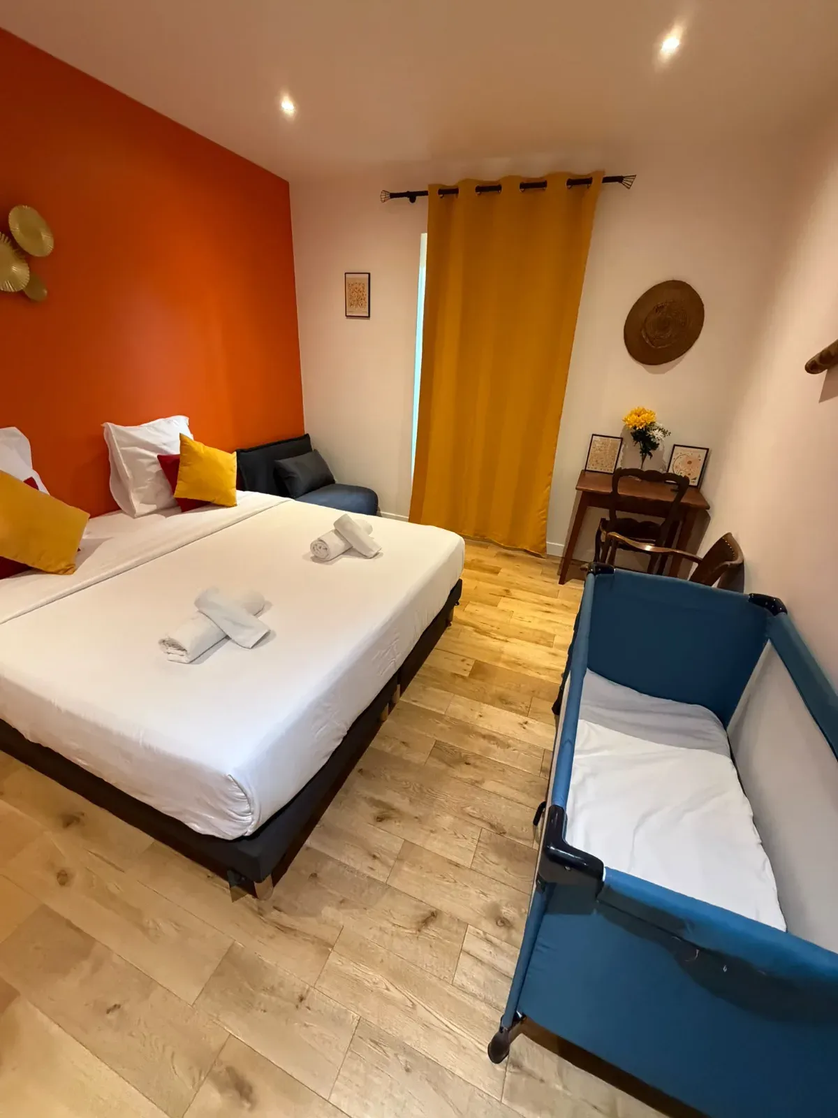 Chambre familiale avec mur orange, grand lit et lit parapluie installé