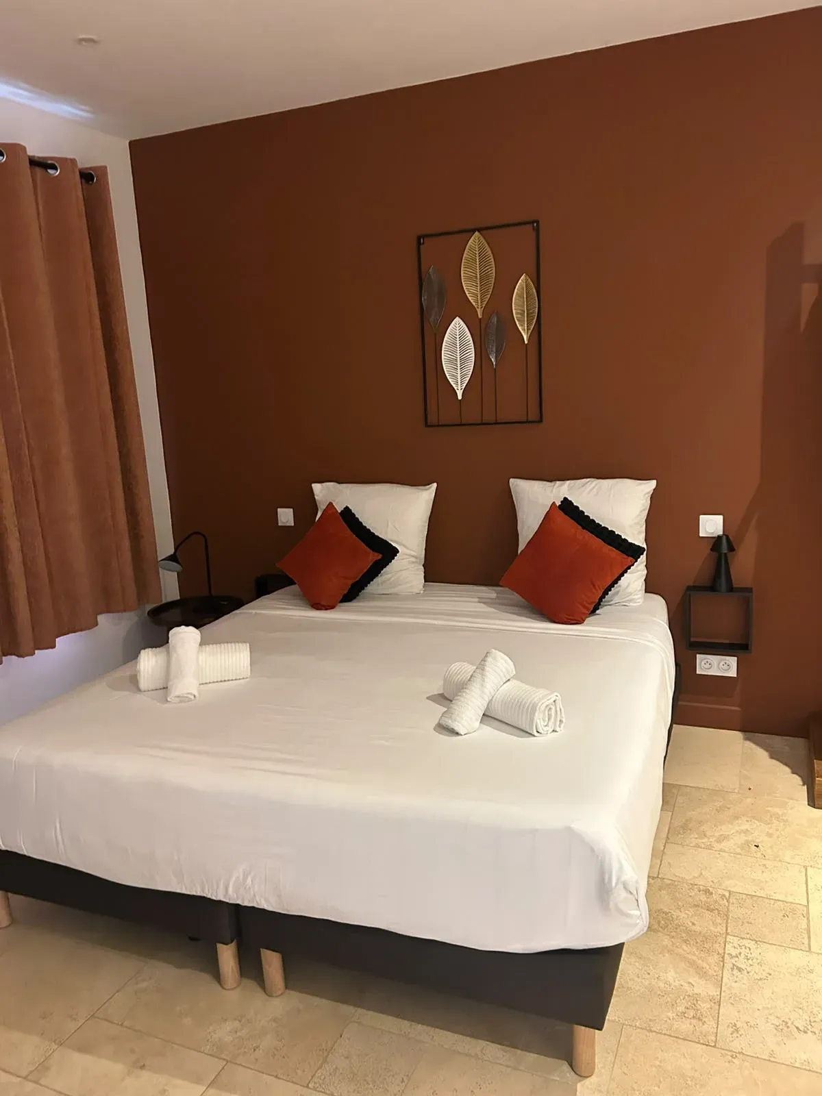 Chambre aux murs terracotta, lit double en linge blanc et serviettes roulées